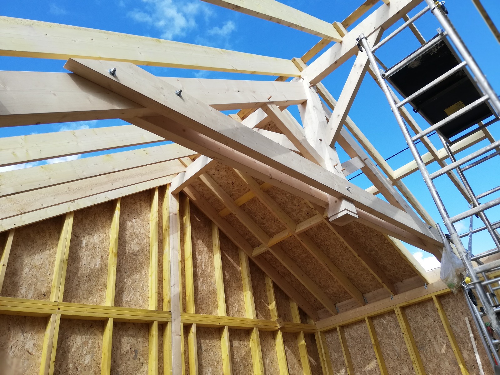 La construction d'un toit avec des pannes de bois dans un environnement de chantier en plein soleil.